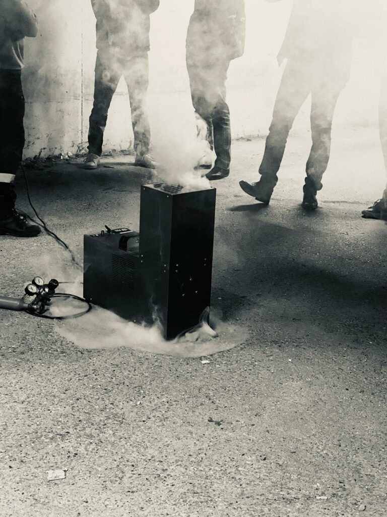 Machine effectuant des essais de fumigènes chauds durant une campagne de test des systèmes de désenfumage, illustrant des nuages de fumée.